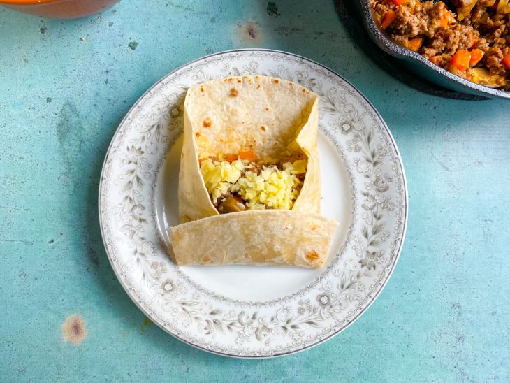 Burrito recheado com carne e queijo sendo fechado.