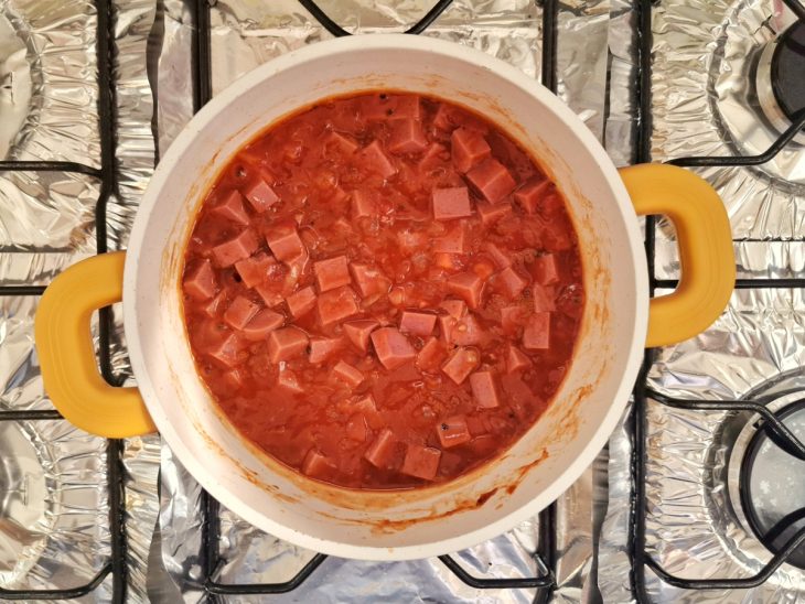 Uma panela com fiambre, molho de tomate e tomate picado.