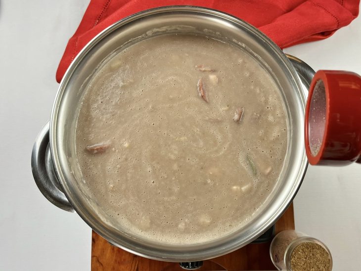 Uma panela com caldo de feijão cozinhando e a adição de tempero.