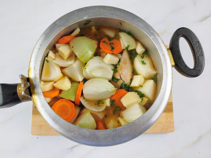 Batatas, cenoura, aipim, cebola, cheiro-verde e água adicionados na panela de pressão com o frango.