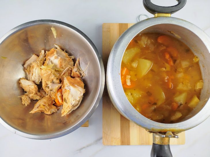 Panela de pressão aberta com os legumes e frango reservado em uma tigela ao lado.