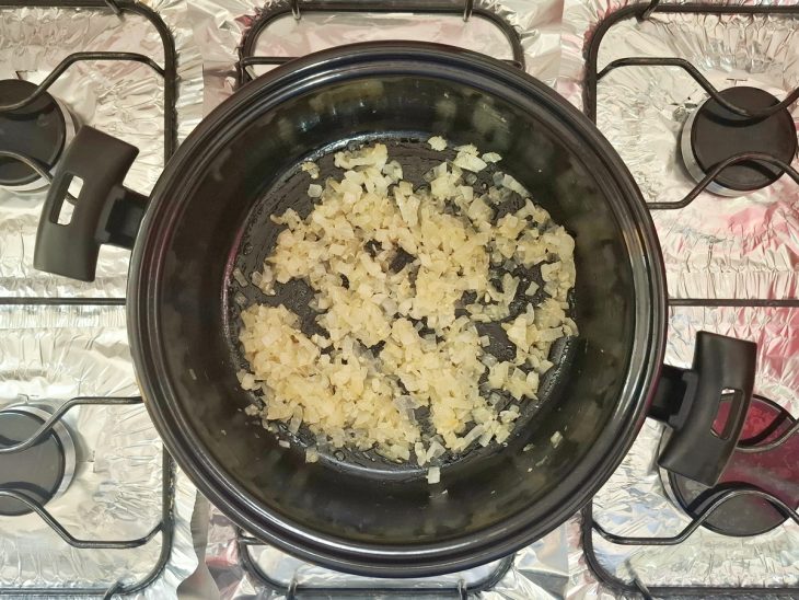 Cebola e alho sendo refogados na manteiga em uma panela no fogão.