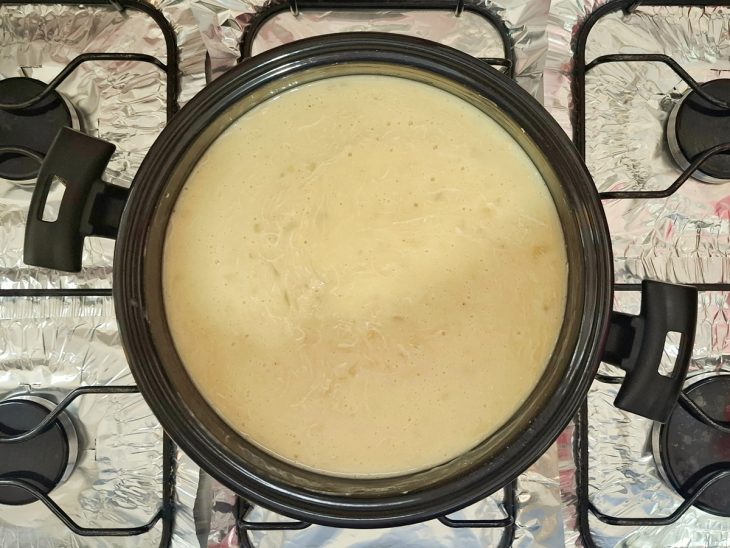 Uma panela com o caldo de mandioca e o frango desfiado no fogão.