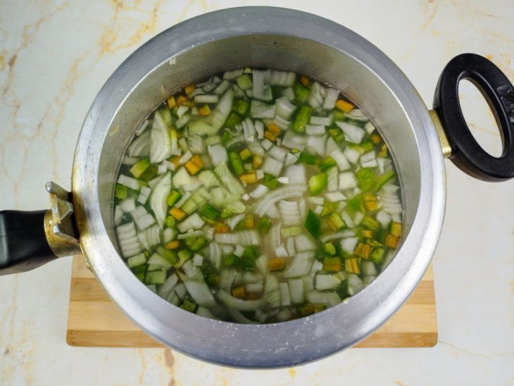 Panela de pressão com ingredientes adicionados e água sobre uma tábua