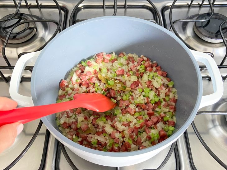 Uma panela com azeite, linguiça, cebola, alho, louro, sal e talos de couve ao fogo.