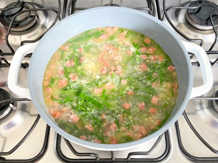 Uma panela com a linguiça temperada, a batata, caldo de galinha e couve ao fogo.