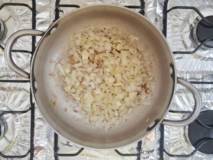 Alho e cebola fritando em uma panela com páprica e pimenta-do-reino.