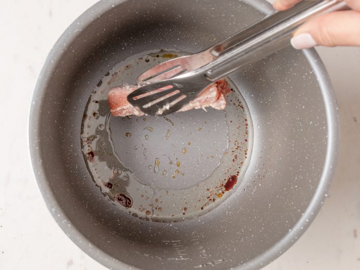 Uma panela com banha, açúcar e costelinhas sendo colocadas por cima.