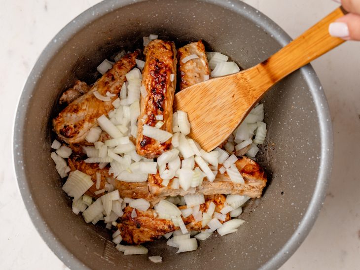 Uma panela com costelinhas e cebolas picadas.