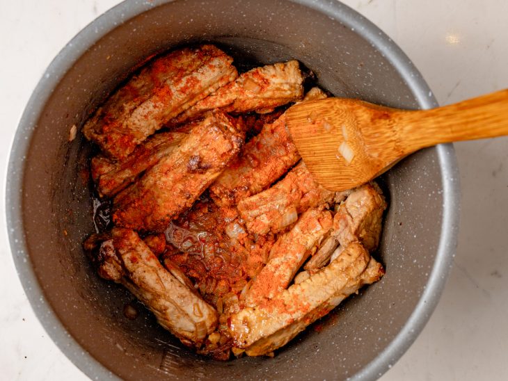 Uma panela com costelinhas, cebolas, colorau e vinho branco.