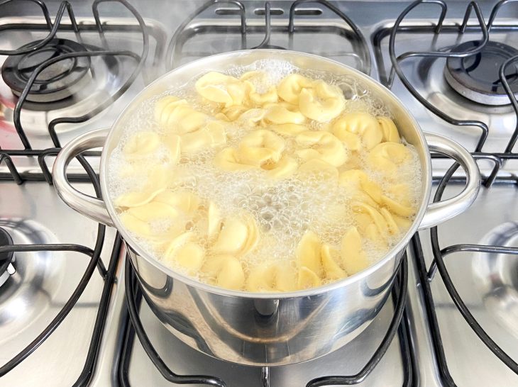 Uma panela com água fervente e macarrão capeletti.