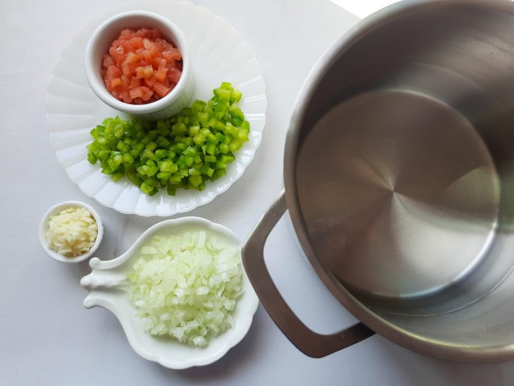 Cebola, alho, pimentão e tomate picados em recipientes e ao lado uma panela