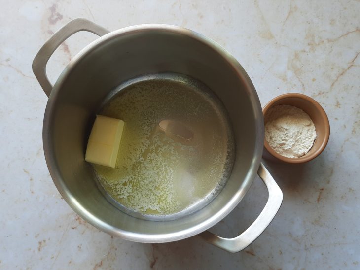 Panela média com manteiga e recipiente com farinha ao lado.