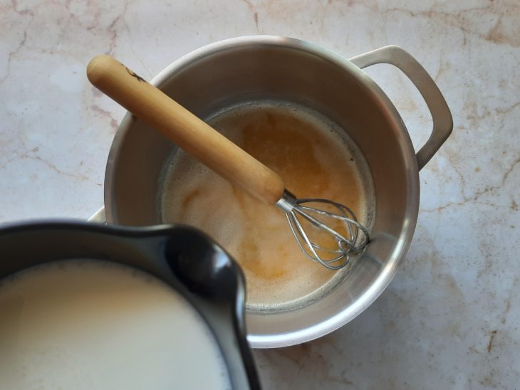 Recipiente com leite para ser despejado na mistura de farinha e manteiga da panela média.