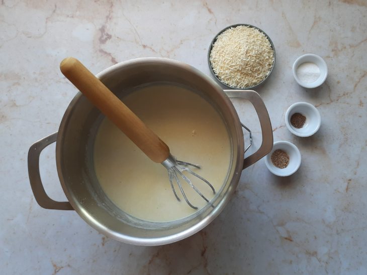 Base do molho branco em uma panela e ingredientes em recipientes ao lado.