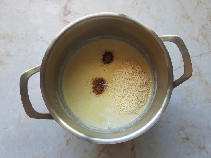 Base de molho branco em uma panela com noz-moscada, queijo parmesão, sal e pimenta-do-reino adicionada.