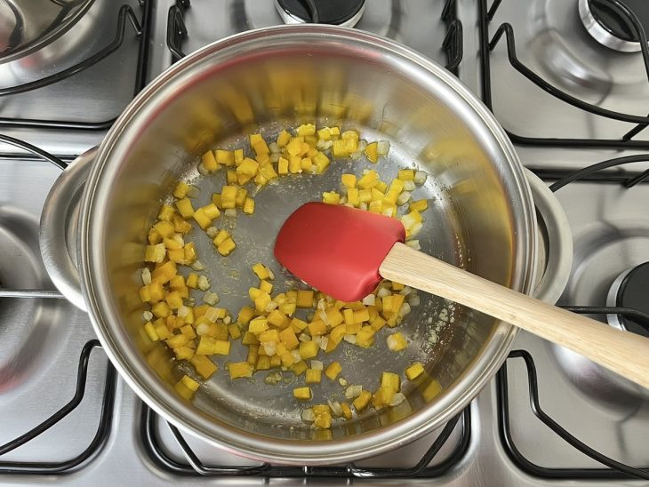 Uma panela refogando alho, cebola e pimentão amarelo.