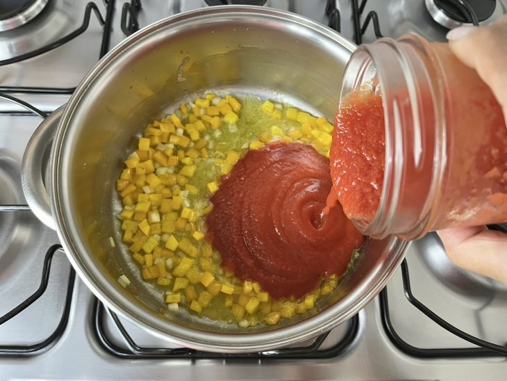 Uma panela refogando alho, cebola e pimentão amarelo com molho de tomate.