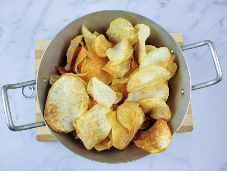 Um escorredor de metal contendo fatias de cará fritas.