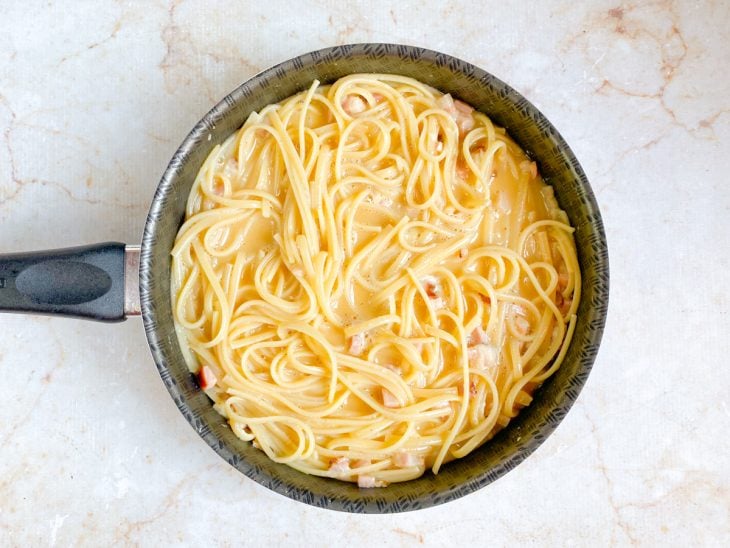 Ovos com parmesão e temperos adicionados na frigideira com macarrão.