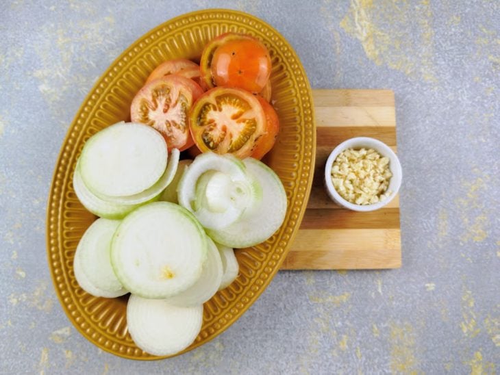 Cebola e tomate picados em um prato, e alho picado em um pote pequeno.