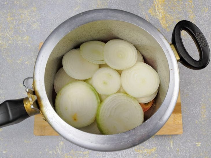 Camada de cebola por cima dos tomates na panela de pressão.