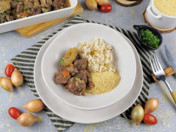 Carne de panela com cebola pronta servida em um prato com arroz e farofa.