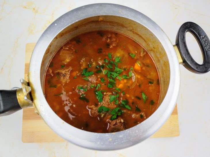 Uma panela com a carne cozida e molho finalizados com cheiro-verde.