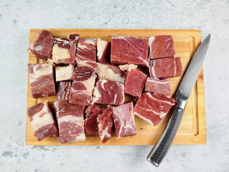 Carne cortada em cubos em uma tabua de madeira.