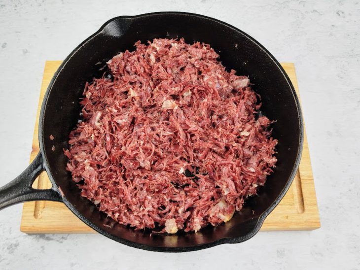 Carne desfiada sendo refogada em uma panela média com óleo.