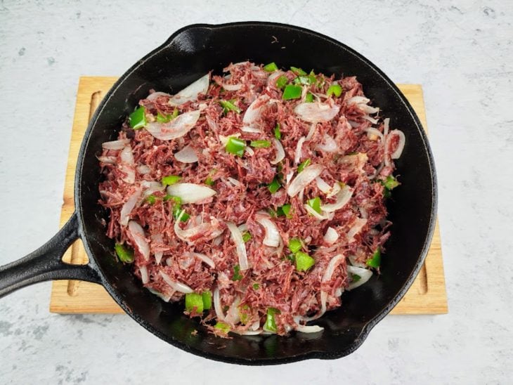 Cebola e pimentão picados adicionados a carne refogada na panela.