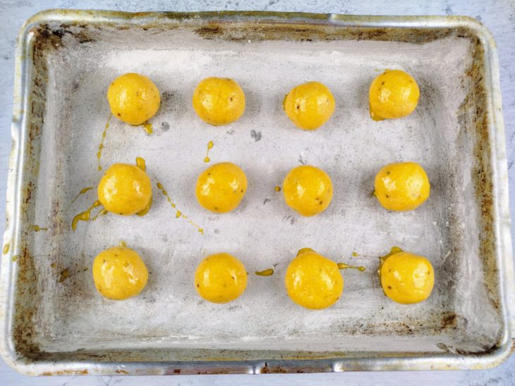 Bolinhas feitas da massa de cavaca pinceladas com gema de ovo em uma forma.