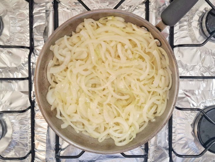 Cebolas fatiadas e temperadas com sal na frigideira.