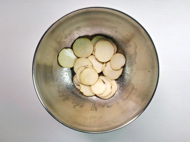 Rodelas de batata-doce fatiadas e temperadas com azeite e sal em um recipiente.