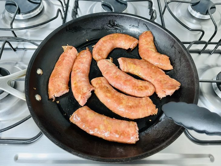 Uma frigideira com linguiça cortada.