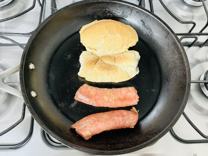 Uma frigideira com linguiça e pão cortados.