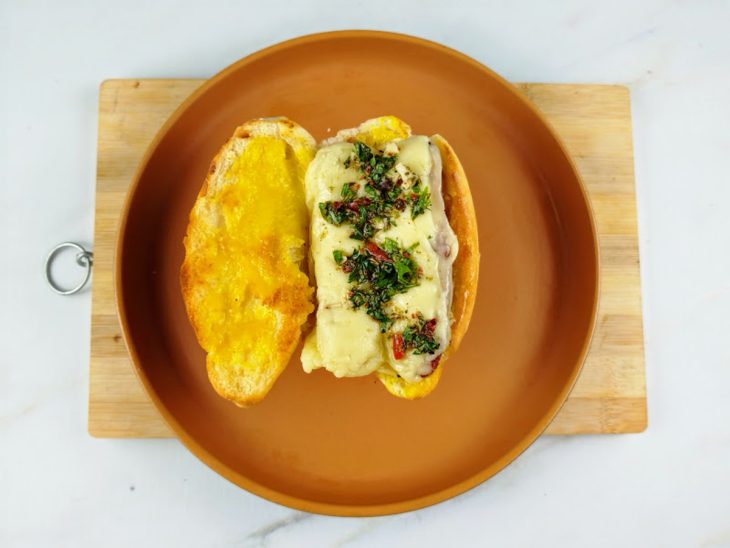 Linguiça e molho chimichurri adicionados no pão com mostarda pincelada.