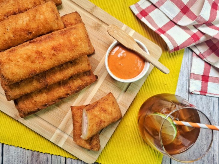 Uma tábua com cigarrete de presunto e queijo, um pote com molho e um copo com chá.