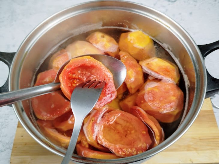 Uma panela cozinhando goiabas com água, açúcar e rama de canela.