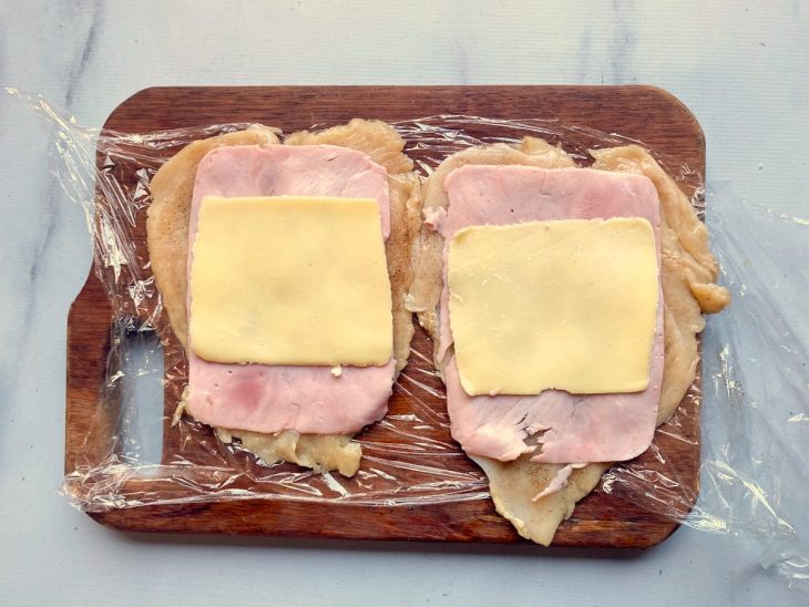 Filés de frango já temperados com uma fatia de presunto e queijo por cima.