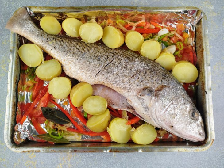 Uma assadeira com o refogado, batatas e o peixe antes de assar.