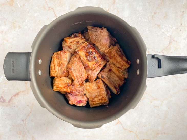 Uma panela de pressão com a costela, cebola e alho caramelizados.