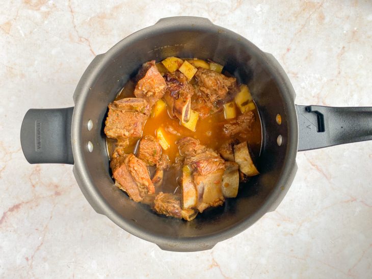 Uma panela de pressão com os ingredientes da costela, molho e batata picada.