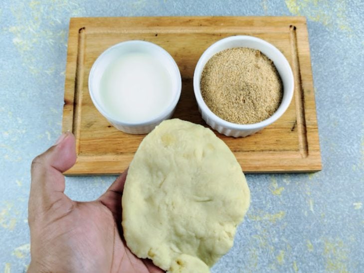 Uma tábua com duas tigelas, uma de leite e outra de farinha de rosca. Na frente, a massa da coxinha.