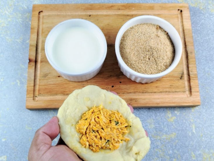 Tábua com duas tigelas, de leite e de farinha de rosca e uma massa de coxinha com recheio no centro.