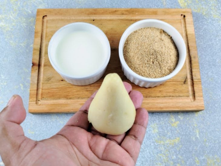 Tábua com duas tigelas, de leite e de farinha de rosca e uma coxinha.