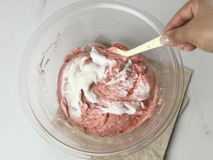 Chantilly sendo adicionado ao creme de morango aos poucos.