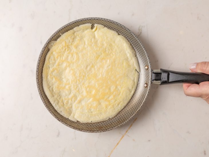 Massa de crepioca na frigideira com o lado dourado para cima.