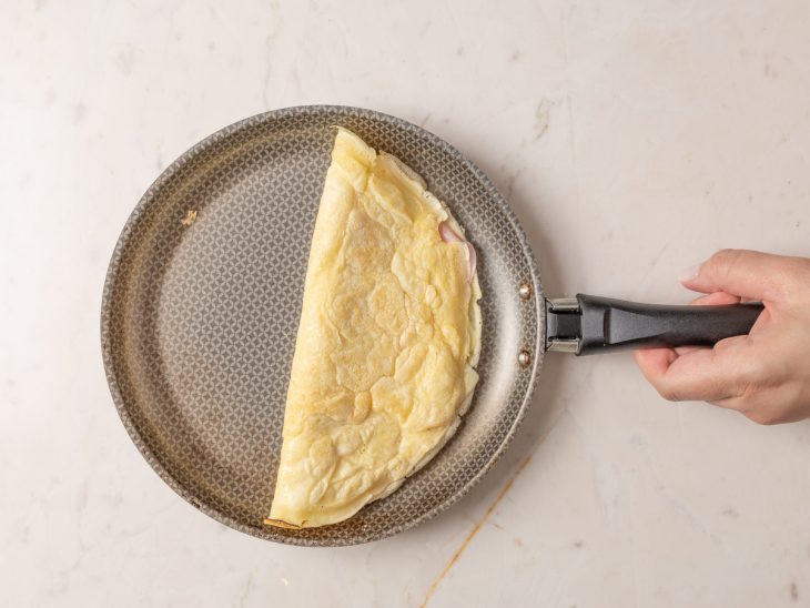 Crepioca recheada com presunto e queijo fechada, ainda na frigideira.