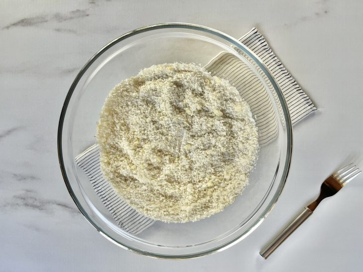 Uma tigela contendo flocão de arroz, açúcar, sal, manteiga, óleo e coco ralado.